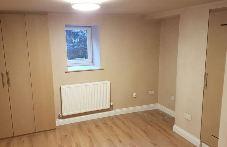 A minimalist room with wooden flooring, beige walls, and a small window.