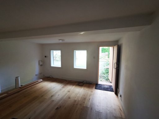 Bright room with wooden floor, three windows, and an open door leading outside.