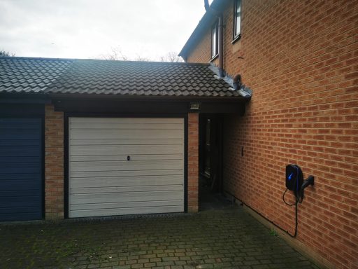 A brick garage with a white door and an electric vehicle charging point.