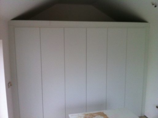 A plain white built-in wardrobe with vertical panels and a sloped roof.