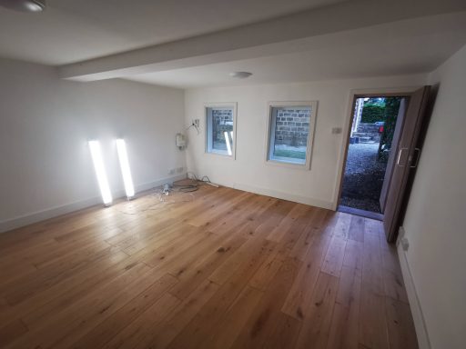 Bright, empty room with wooden floors and an open door leading outside.