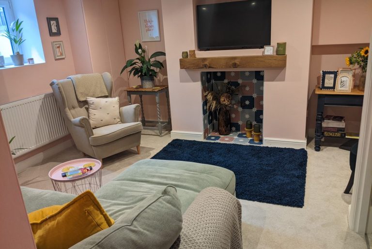 Cozy living room with a pink wall, TV, armchair, and stylish fireplace.