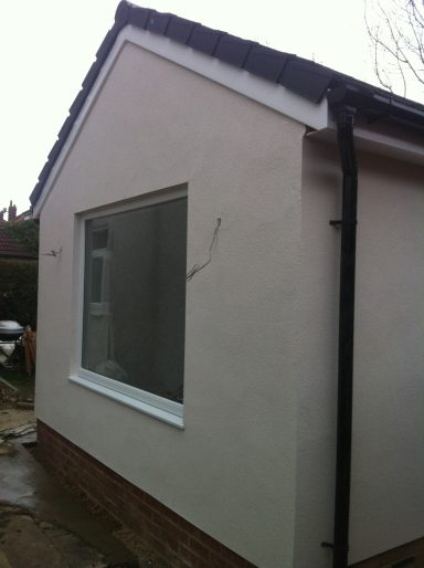 Corner of a house with a large window and freshly plastered exterior wall.