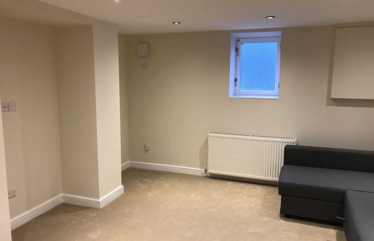 TV room with light beige walls, a window, and a black sofa in the corner.