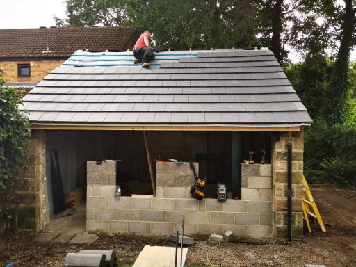 A worker installs roof tiles on a building under construction.