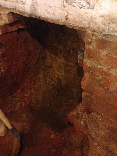 Excavation site showing a deep hole in a brick wall with disturbed soil.