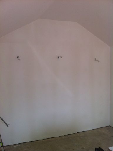 Empty room with a sloped wall painted white, featuring three hooks mounted on it.