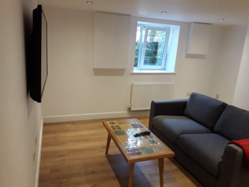 Modern living room with a grey sofa, wooden coffee table, and a window with light streaming in.