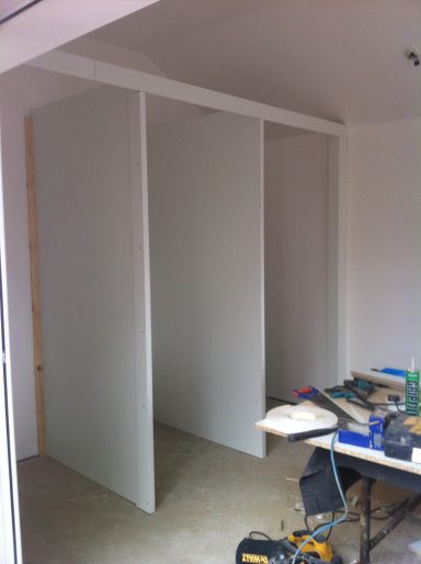 Interior space with unfinished white partitions and tools scattered on the floor.