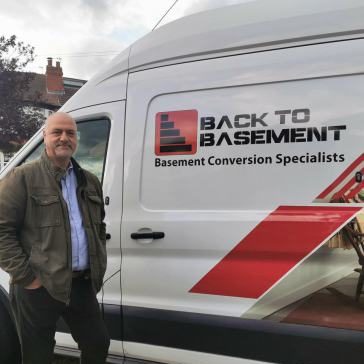 Rubi Kasuto stands beside a van marked "Back to Basement - Basement Conversion Specialists."