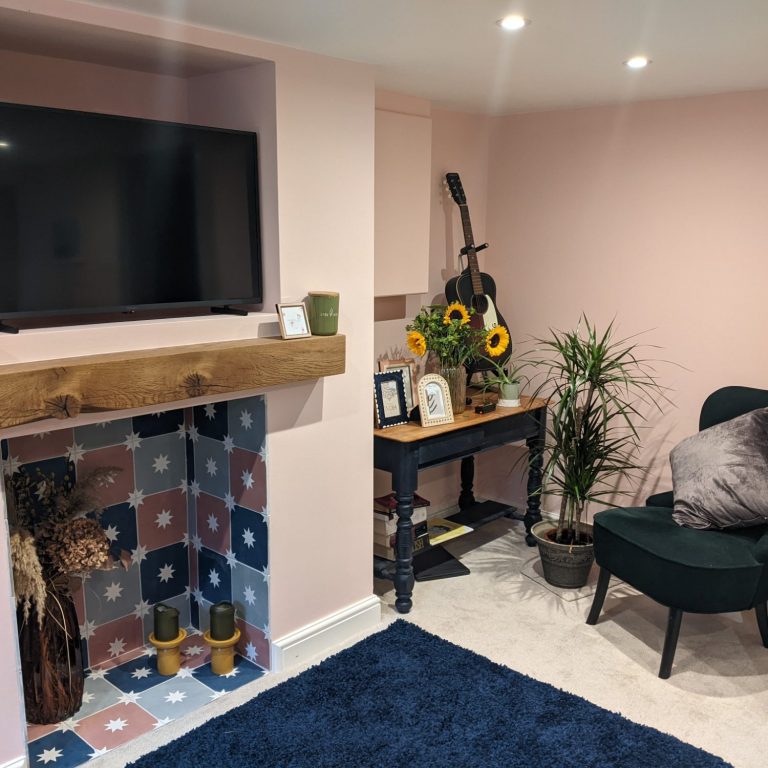 Cozy living room with a TV, plants, sunflowers, and a comfortable chair against pink walls.