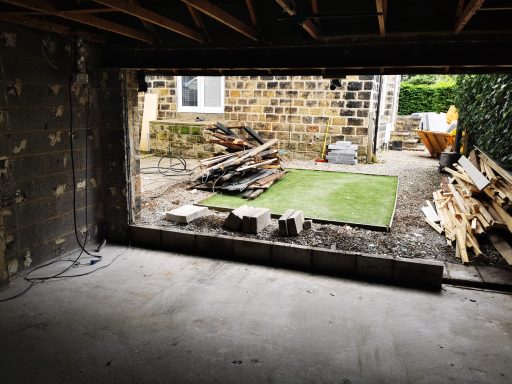 View of an unfinished interior opening to a garden, with construction materials nearby.