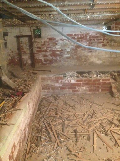 A partially finished basement with exposed brick walls and debris on the floor.