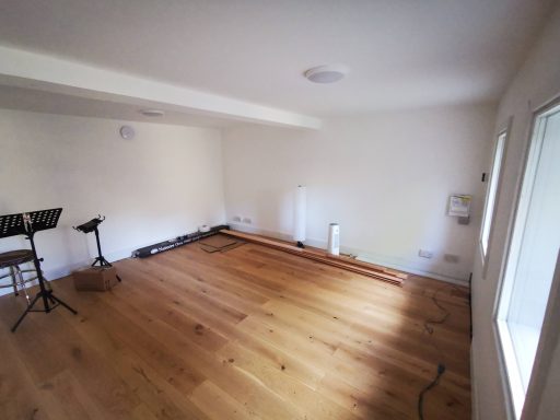 Empty room with wooden flooring, white walls, and a small music stand in the corner.