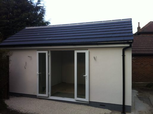 Modern building with a flat roof and large glass doors, set in a suburban area.