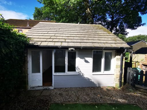 A small house with a stone exterior, grey walls, and green surroundings.